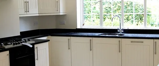A kitchen with white units, black worktops and a window over the sink