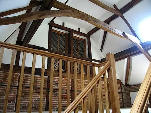 Inside a converted barn: an oak gallery and staircase below the old roof timbers